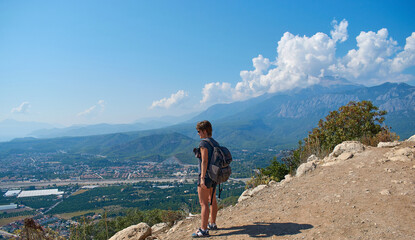 A tourist stands on a mountain and looks at the landscape of the city and mountains