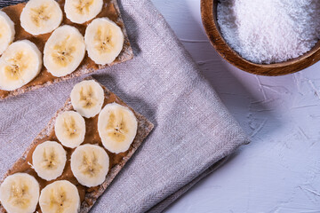 Multi seed crispbread with banana's slices, peanut butter and coconut on white background. Swedish and healthy snack. Top view.