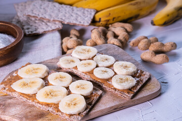 Multi grain crispbread with banana's slices and peanut butter on a wooden table. Swedish snack. Close up view.