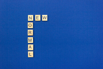 The phrase New Normal made of wooden blocks on blue cardboard background. Layout, top view, place for text.