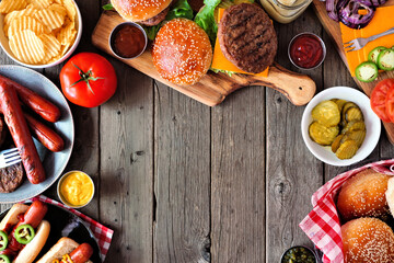 Summer BBQ food frame with hot dog and hamburger buffet. Above view table scene over a dark wood background. Copy space.