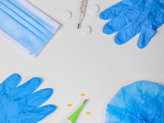 medical gloves, mask, pills, two thermometers and a hat on a white background with a place for text in the middle, top view close-up.
