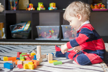 Cute little baby boy having fun at home playing with colorful wooden blocks, on the floor.