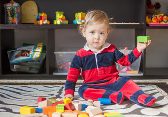 Cute little baby boy having fun at home playing with colorful wooden blocks, on the floor.