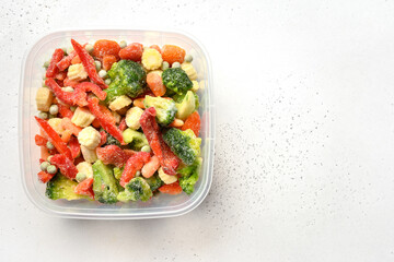 Frozen colorful vegetables in container on white background. View from above.