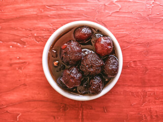 Delicious sweet grooselha with syrup on white bowl. Red background.