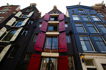 Close up image of Amsterdam's traditional narrow and tall houses with vibrant colored brick facades which harbor decorative elements including flower pots and colorful wooden window shutters. 