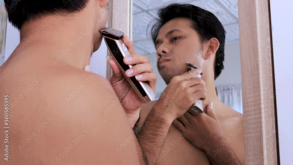 Wall mural Young Asian man shaves with an electric shaver, Concept Stay home 