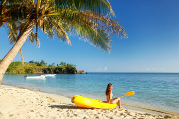 Fototapeta na wymiar Young woman relaxing on top of sea kayak on the beach