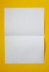 Folded white paper on yellow background .