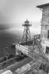 Alcatraz island and prison exterior at dusk showing guard tower and fog in black and white