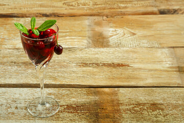 Crystal glass with cherry juice and fresh berries inside on a wooden table.