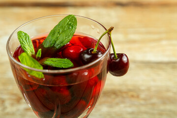 Crystal glass with cherry juice and fresh berries and mint inside on a wooden table.