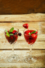 Crystal glass with cherry juice and strawberry and fresh berries and mint inside on a wooden table. Copy space.