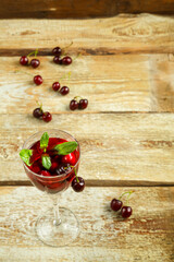 Crystal glass with cherry juice and fresh berries and mint inside on a wooden table and berries on the table.
