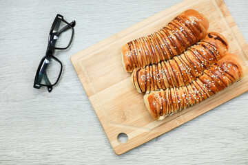 View from above of loaves of red bread on chopping board and eyeglasses on wooden table 