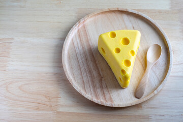 A cheese cake looks like real Swiss cheese in a wooden plate on wood table. Cheese cake concept
