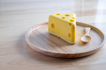 A cheese cake looks like real Swiss cheese in a wooden plate on wood table. Cheese cake concept