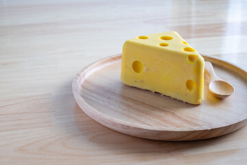 A cheese cake looks like real Swiss cheese in a wooden plate on wood table. Cheese cake concept