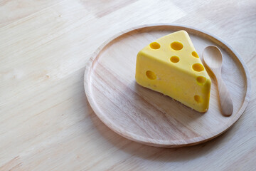 A cheese cake looks like real Swiss cheese in a wooden plate on wood table. Cheese cake concept