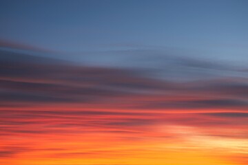 Naklejka na ściany i meble Intense, radiant orange cirrus clouds at dawn against a deep blue sky.