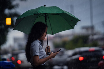 Asian woman use the umbrella while it rains She is walking across the street. And use the phone