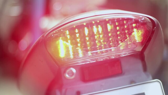 the motorcycle stands on the sidestand in the room. This is a sport bike with lots of purple plastic. you see the back of the motorcycle with a taillight and a turn signal that flashes