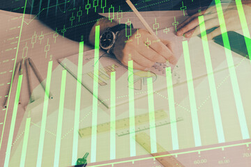 Double exposure of man's hands writing notes of stock market with forex chart.