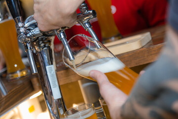 Filling glass with beer. Bartender hand at beer tap pouring draught beer in glass serving in restaurant or pub. Close-up of male barman hand at beer tap pouring lager beer at restaurant or bistro.
