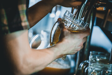 Hand of man pouring tankard of frothy draught beer from stainless steel beer tap in bar or pub into large glass tankard. Bartender at beer tap pouring beer in glass serving in restaurant.