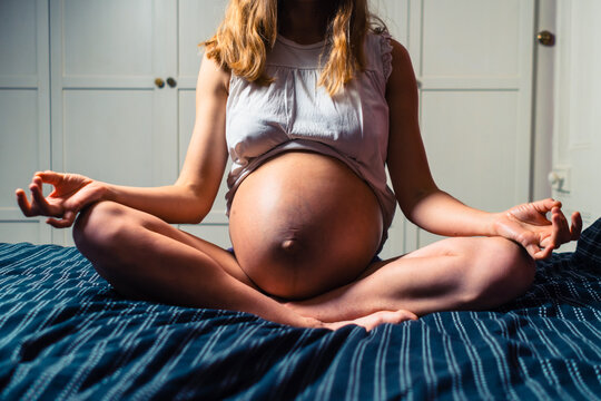 Young pregnant woman in meditative pose on a bed