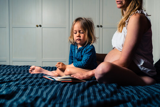 Young pregnant mother reading to her preschooler on a bed