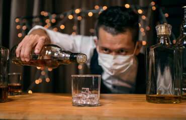Barman pouring whiskey wearing  protective mask on the bar counter 