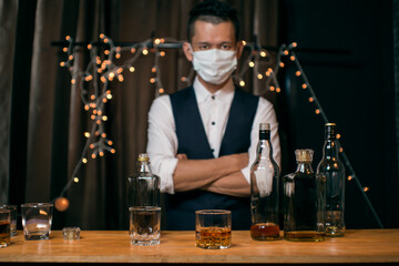 Barman pouring whiskey wearing  protective mask on the bar counter 