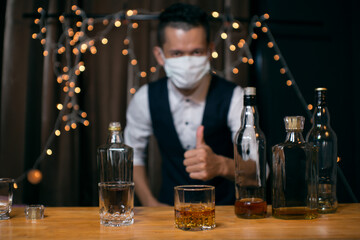 Barman pouring whiskey wearing  protective mask on the bar counter 