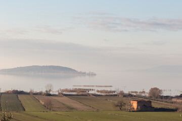 A view of Trasimeno lake and Isola Polvese (Umbria, Italy) with mist and cultivated fields on the foreground