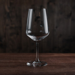 Empty wine glass on wooden table against dark background in bar. Crystal clear wine glass with traditional round goblet shape and slim stem on wood counter top bar with blurry background scene