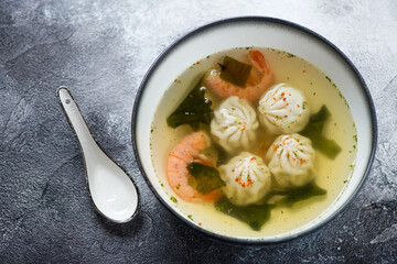 Bowl of panasian dumpling and prawn soup over grey and white stone background, horizontal shot, selective focus