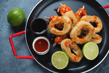 Fried breaded calamari rings and crab claws with lime and dips on a serving pan, elevated view, close-up, horizontal shot