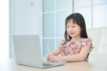 Little asian schoolgirl online learning with laptop at home. Education and distance learning for kids. Homeschooling during quarantine.