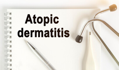 On the table are a stethoscope, a thermometer, a pen and a notebook with the inscription -Atopic dermatitis