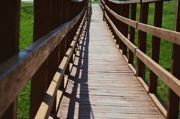 Obraz premium Bridge wooden hanging against the backdrop of green grass on a summer sunny day