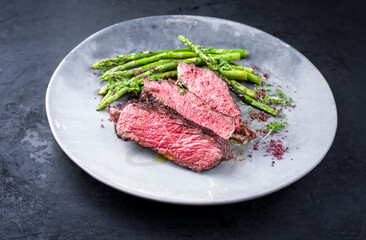 Barbecue dry aged wagyu rib-eye beef steak with green asparagus and red wine salt as closeup on a modern design plate