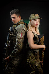 Fototapeta premium a girl and a guy in military overalls pose with an airsoft gun on a dark background