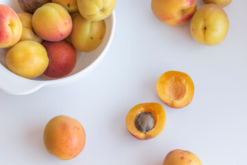 Some fresh apricots on a white background. One apricot is cut in half