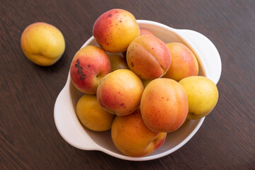 Ripe apricots in a white bowl on a brown table
