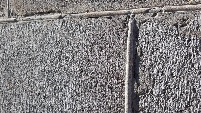 Wall of gray cinder block with old seams. The facade of the building on a sunny day. Perspective view