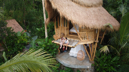 An Asian couple on hammock balcony of bamboo tree house. House in tropical forest.