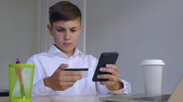 Beautiful Boy 10 Years Old Sitting At Home Makes Online Payments Through The Internet From Bank Card On Smartphone. Child Makes Purchases In The Online Store. Online Banking With Smart Phone.