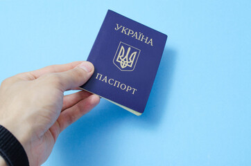 Ukrainian passport on a blue background. Man's hand holds a Ukrainian passport in hand, gives the passport . The passport of the citizen of Ukraine in the macro. Passport General plan and close-up